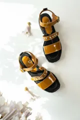 Sandalias de cuero color suela con acabado charolado, diseño de tiras con tachas metálicas y hebilla ajustable. Poseen una suela de goma negra tipo track con plataforma.