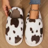 Pantuflas sin talón confeccionadas en algodón afelpado y piel sintética, con divertido estampado de manchas de vaca en tonos blanco y marrón, y suela de PVC.