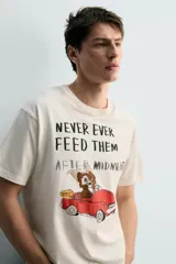 Camiseta de corte relajado color crudo, con cuello redondo y manga corta. Presenta un estampado frontal con una ilustración de Gizmo de la película Gremlins conduciendo un auto rojo y el texto 'Never ever feed them after midnight'.