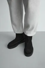 Bota de caña corta fabricada en piel con acabado serraje, con detalle de costura en el empeine, forro interior de pelo sintético y suela plana a tono.