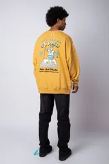Buzo de cuello redondo y corte oversize, confeccionado en tela rústica color amarillo. Presenta un pequeño estampado central en el pecho con un avión y olas.