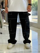 Pantalón cargo de jean negro con múltiples bolsillos utilitarios y costuras visibles en contraste de color blanco.