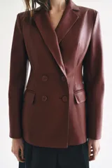 Blazer de cuero sintético en color beige, con cuello solapa, manga larga y bolsillos con solapa en el frente. Cierre frontal cruzado con botones a tono.