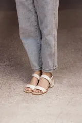 Sandalia de cuero color beige claro (off white) con taco ancho y tiras finas ajustables con hebilla metálica dorada en el tobillo.