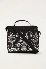 Bolso tipo lonchera o cooler de la marca Farm Rio, color negro con estampado floral y tropical en blanco. Cuenta con cierre superior con cremallera, bolsillo frontal con cierre, asa de mano superior y correa ajustable para colgar al hombro o cruzado.