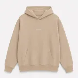 Canguro con capucha de calce oversize, confeccionado en tejido pesado color gris claro. Presenta un bordado minimalista con la palabra 'ASCEND' en la parte superior trasera, puños y ruedo acanalados.