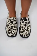 Mocasín de cuero con pelo y estampado de vaca en blanco y negro. Presenta horma cuadrada, diseño enrejillado en la capellada y taco bajo de 4,5 cm.
