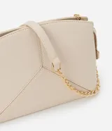 Cartera bandolera pequeña de diseño estructurado en color beige, confeccionada en poliuretano con acabado liso. Presenta un diseño geométrico con costuras en relieve en la parte frontal, cierre superior con cremallera y una elegante correa de cadena metálica en tono dorado.