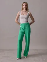 Pantalón largo de crepe elastizado color verde, de corte recto, con bolsillos delanteros y apliques de botones metálicos.