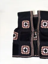 Chaleco sin mangas, confeccionado con cuadrados de cuero negro perforado combinados con cuadrados de crochet en hilo de algodón negro y blanco, con detalles centrales en rojo.