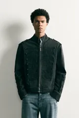 Chaqueta cropped fit de denim de algodón en color negro con efecto lavado, cuello mao y cierre frontal con cremallera. Presenta aplicaciones de trabillas horizontales en el pecho y en las mangas, además de hombreras abotonadas.