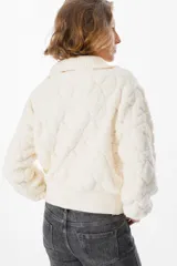 Sweater de tejido acolchado con diseño de rombos, color beige, con cuello polo y cierre frontal parcial. Presenta puños y cuello en tejido acanalado, con mangas largas y corte cropped.