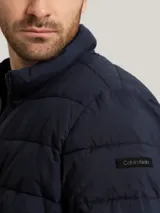 Campera puffer azul marino con cierre frontal, cuello alto y bolsillos laterales con cierre. Logo de Calvin Klein en la manga.