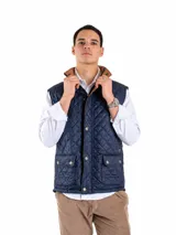 Chaleco azul marino acolchado con diseño capitoneado en rombos, cuello alto forrado en tono tostado y bolsillos frontales con solapa y botones. Cuenta con cierre frontal y detalles de broches metálicos.