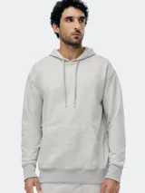 Buzo con capucha de corte holgado, confeccionado en tejido de punto color gris melange. Presenta bolsillo frontal tipo canguro, cordones ajustables en la capucha y puños y ruedo acanalados.