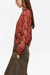 Camiseta de manga larga confeccionada en tejido de tul semitransparente con estampado animal print abstracto. Presenta cuello redondo, corte ajustado y detalles de frunces laterales que aportan textura y movimiento a la prenda.