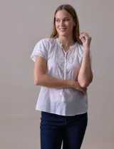 Blusa blanca de algodón marca Cupio, con cuello a la base, escote en V y lazo de ajuste. Presenta bordado en la parte delantera y mangas cortas amplias con aplique de puntilla.