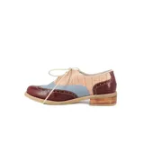 Zapato tipo Oxford de cuero color beige con detalles en charol negro y blanco, con cordones negros y taco bajo de madera.