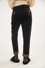 Pantalón recto de tiro medio confeccionado en pana con lycra. Presenta pinzas frontales, bolsillos laterales y traseros, y cierre con botón dorado. El diseño destaca por el detalle de paño espigado en el interior del ruedo, visible al doblarlo, y un pin bordado decorativo en el bolsillo delantero.