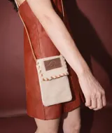 Mini bolso de gamuza color arena, con solapa y cierre de velcro. Presenta un detalle de costura decorativa en los bordes y una etiqueta de cuero con el logo "Sierra Mora". Incluye una correa fina para llevar al hombro o cruzado.
