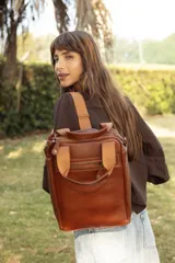 Matera mochila unisex de cuero marrón, con diseño estructurado, bolsillo frontal con cierre, asas superiores y correas ajustables.