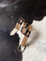 Cinto de cuero marrón claro con detalles bordados geométricos en tonos azul, rojo y beige, hebilla metálica de bronce y puntera forrada en cuero.