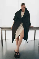 Trench oversize de corte largo confeccionado en mezcla de algodón con estampado de microcuadros. Presenta cuello alto, cierre frontal con botones, mangas largas con trabillas ajustables y bolsillos laterales.