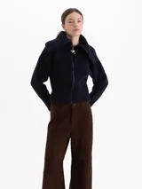 Cardigan de tejido tipo corderito en color azul marino, con cuello alto, cierre frontal con tirador metálico en forma de fresa y mangas largas.