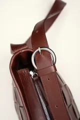 Cartera tipo morral de cuero color beige, con diseño trenzado artesanal, correa larga regulable y cierre superior.