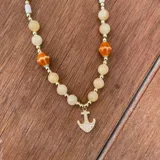 Collar de piedras naturales en tonos amarillos, con cuentas de cerámica naranja estampadas, abalorios dorados y dije central de ancla con pavé de circones.