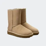 Botas de caña media UGG Classic Short II, confeccionadas en piel de oveja de doble cara color beige, con forro interior de lana suave y suela exterior liviana para mayor amortiguación.