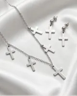 Set de joyería en acero quirúrgico compuesto por un collar de cadena fina con seis dijes de cruz colgantes y un par de caravanas a juego con diseño de cruz.