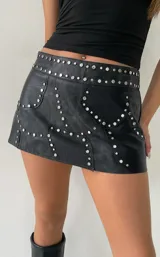Minifalda de cuero sintético negro con diseño de paneles y detalles de tachas metálicas plateadas distribuidas por toda la prenda.