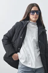 Campera puffer negra con diseño acolchado, capucha integrada y cierre frontal con botones a presión. Presenta puños elásticos y costuras decorativas en el frente.