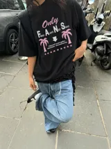 Remera oversize marrón con estampado gráfico frontal en tonos celestes y blancos con la leyenda "Only Fans", palmeras y estrellas.
