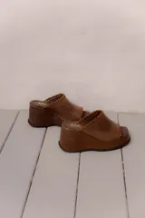 Sandalias de plataforma color marrón, con diseño de una sola tira ancha con detalle de costuras expuestas en los bordes y punta cuadrada.