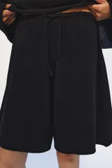Bermuda de algodón color negro, con tiro medio, cintura elástica ajustable con cordones y bolsillos laterales ocultos en costura.