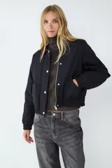 Campera corta de estilo casual, color negro, con cuello de pana en tono contrastante. Presenta cierre frontal con botones a presión, bolsillos laterales, y puños y bajo con acabado elástico.