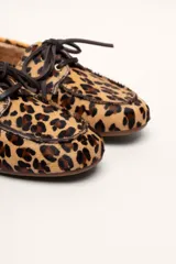 Mocasín tipo boat shoe color marrón, confeccionado en cuero, con cordones de cuero marrón y cordones decorativos azules.