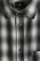 Camisa de corte relajado, confeccionada en mezcla de algodón suave con diseño a cuadros difuminados en tonos negro y blanco. Cuenta con cuello inglés, cierre frontal de botones, bolsillo en el pecho y mangas largas con puños abotonados.