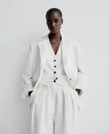 Blazer recta color blanco de lino europeo y viscosa responsable, con solapa, manga larga con hombreras, tres botones en puño, cierre de dos botones y bolsillos de vivo con solapa en delantero.