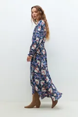 Maxi vestido azul marino con estampado floral en tonos blanco, rosa y azul. Diseño cruzado con lazo en la cintura y mangas largas.