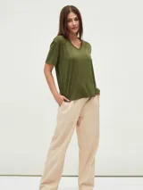 Remera blanca de manga corta con cuello en V y apliques de tachas metálicas doradas dispuestas en forma de V invertida en la zona de los hombros.