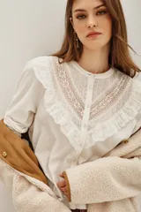 Camisa de algodón y lino color crudo, con cuello redondo, cierre frontal de botones y detalles de encaje y volados en el pecho.