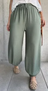 Pantalón tipo babucha de color verde militar, con cintura elástica fruncida y cordón ajustable. Cuenta con diseño amplio y puños elásticos en los tobillos.