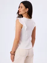 Musculosa blanca sin mangas con detalles de volados bordados en los hombros, confeccionada en tejido texturizado con escote redondo.