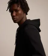 Buzo deportivo negro con capucha, cierre frontal con cremallera, bolsillos laterales y puños ajustados. Confeccionado en tejido de algodón y poliéster.