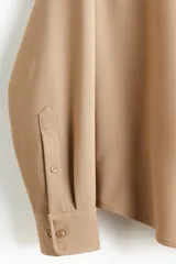 Camisa de manga larga color camel, confeccionada en sarga suave, con cuello americano y tapeta clásica con botones. Presenta canesú en la espalda y bajo redondeado.