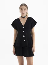 Cardigan de tejido de punto con textura acanalada, color negro, de manga corta y corte entallado. Presenta un escote en V y cierre frontal con botones decorativos de pedrería.