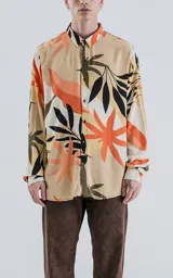 Camisa de manga larga con cuello y botones frontales, confeccionada en rayón con un estampado de hojas tropicales en tonos beige, naranja, negro y verde oliva.